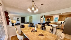 Un grand espace dédié à la salle à manger, avec une longue table en bois entourée de chaises, et une cuisine en arrière-plan.