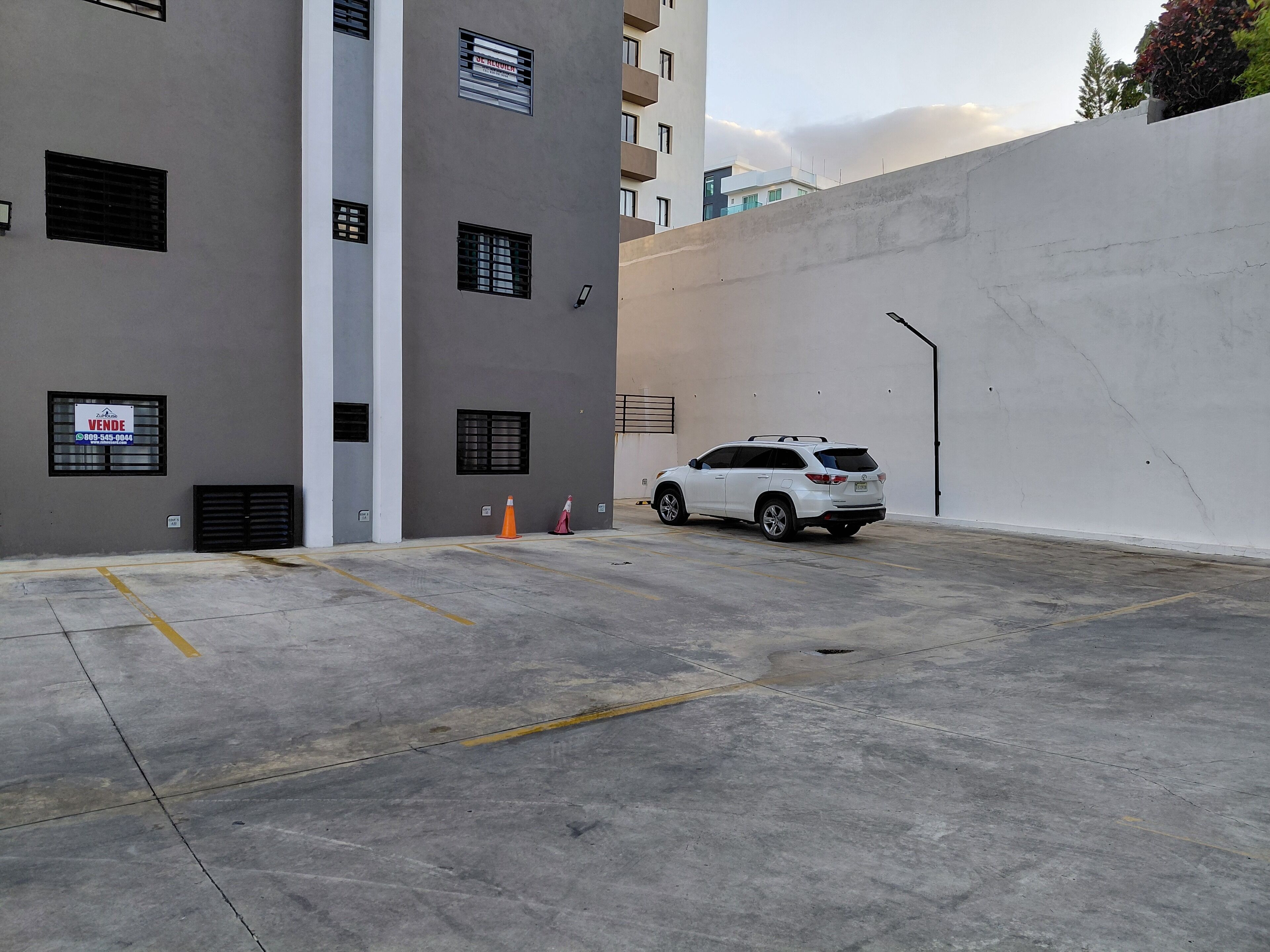 Un espace de stationnement avec un VUS blanc, un bâtiment doté de nombreuses fenêtres et d’une enseigne, et un mur en béton.