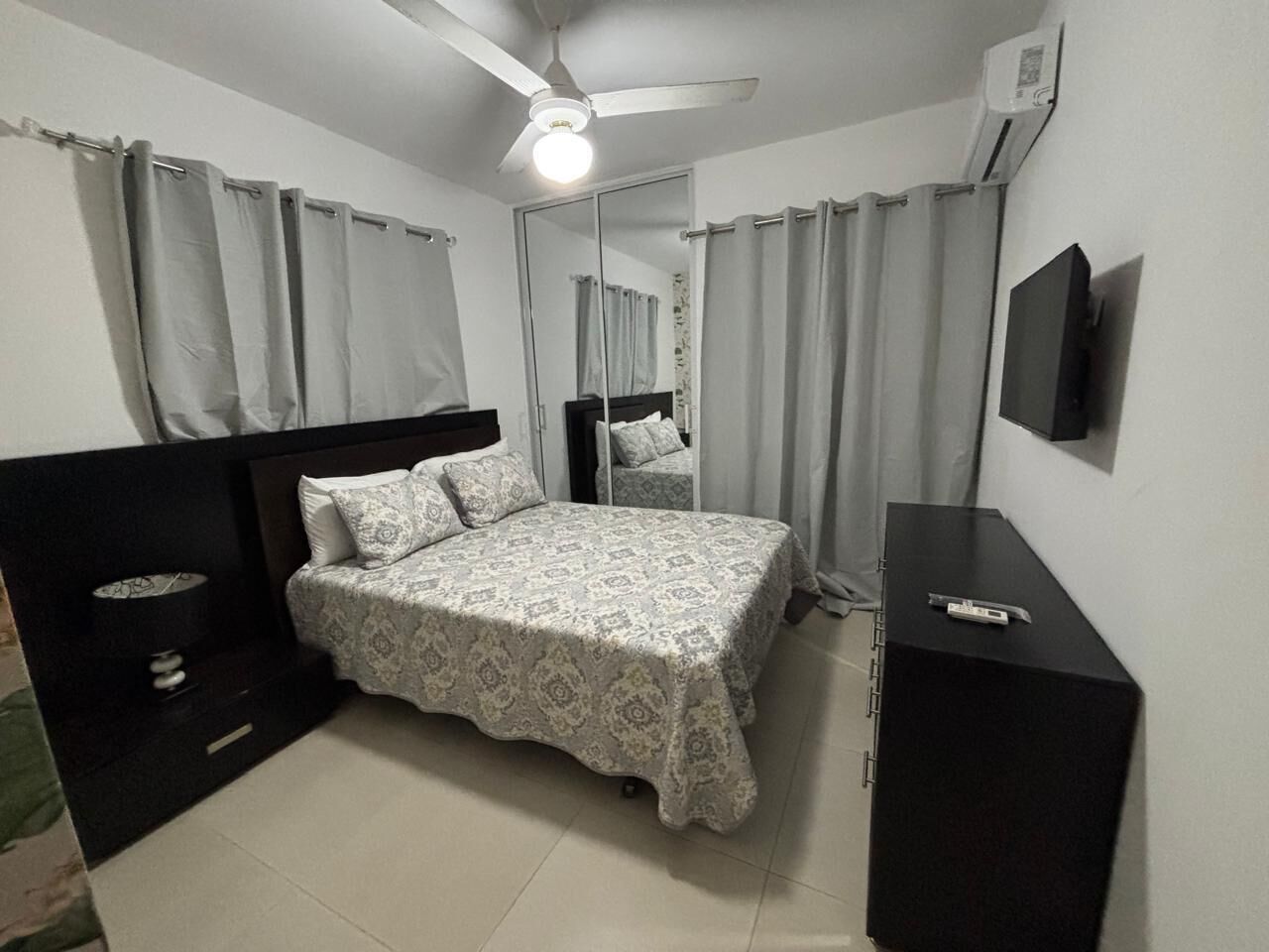 A bedroom with a bed, a nightstand, a dresser, a ceiling fan, and a TV.