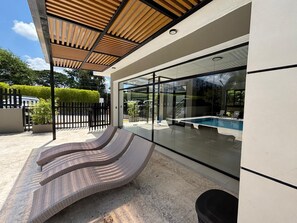A modern outdoor area with a pool, glass walls, and a covered seating area. - cipres (Puñal)