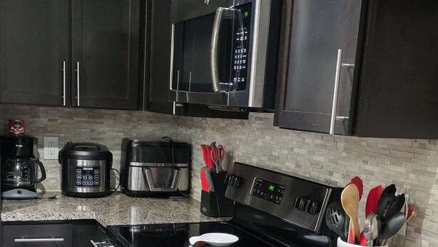Una cocina moderna con electrodomésticos de acero inoxidable, encimeras de granito y armarios negros.
