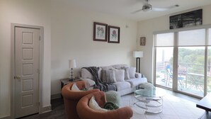 Una sala de estar moderna con un sofá gris, dos sillones, una mesa de centro de vidrio y vistas al exterior a través de amplios ventanales.