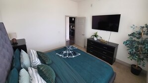 Un dormitorio con una cama, un tocador, un televisor y una planta en maceta.