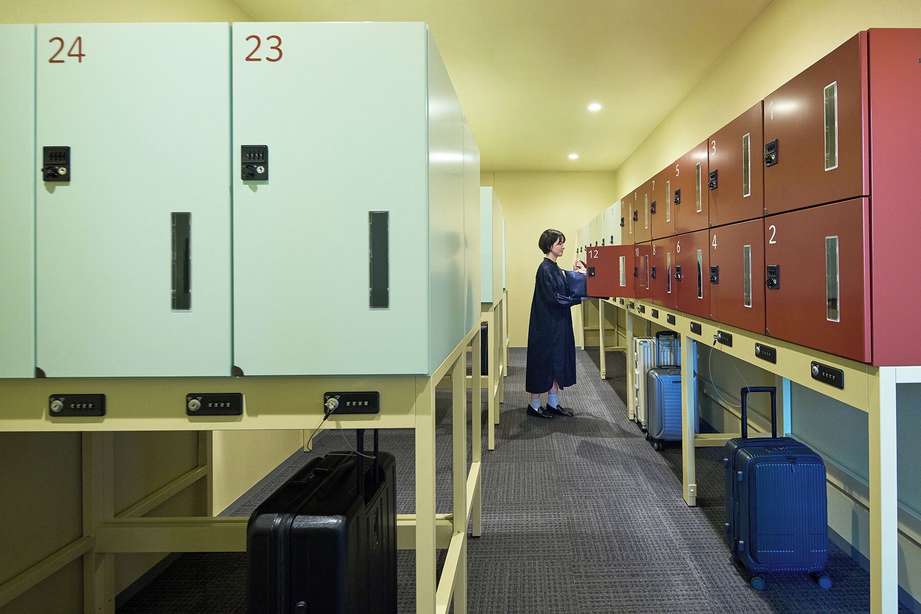A hotel corridor with lockers numbered 23 and 24, and a person standing near lockers 12 and 13.