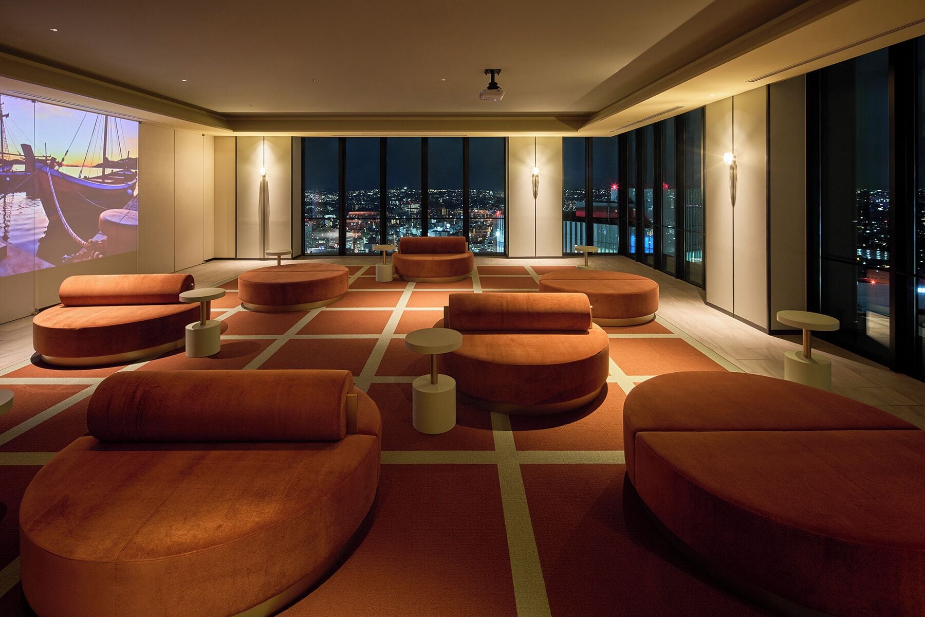 Eine moderne Lounge mit orangefarbenen Sitzgelegenheiten und großen Fenstern mit Blick auf die Stadt.
