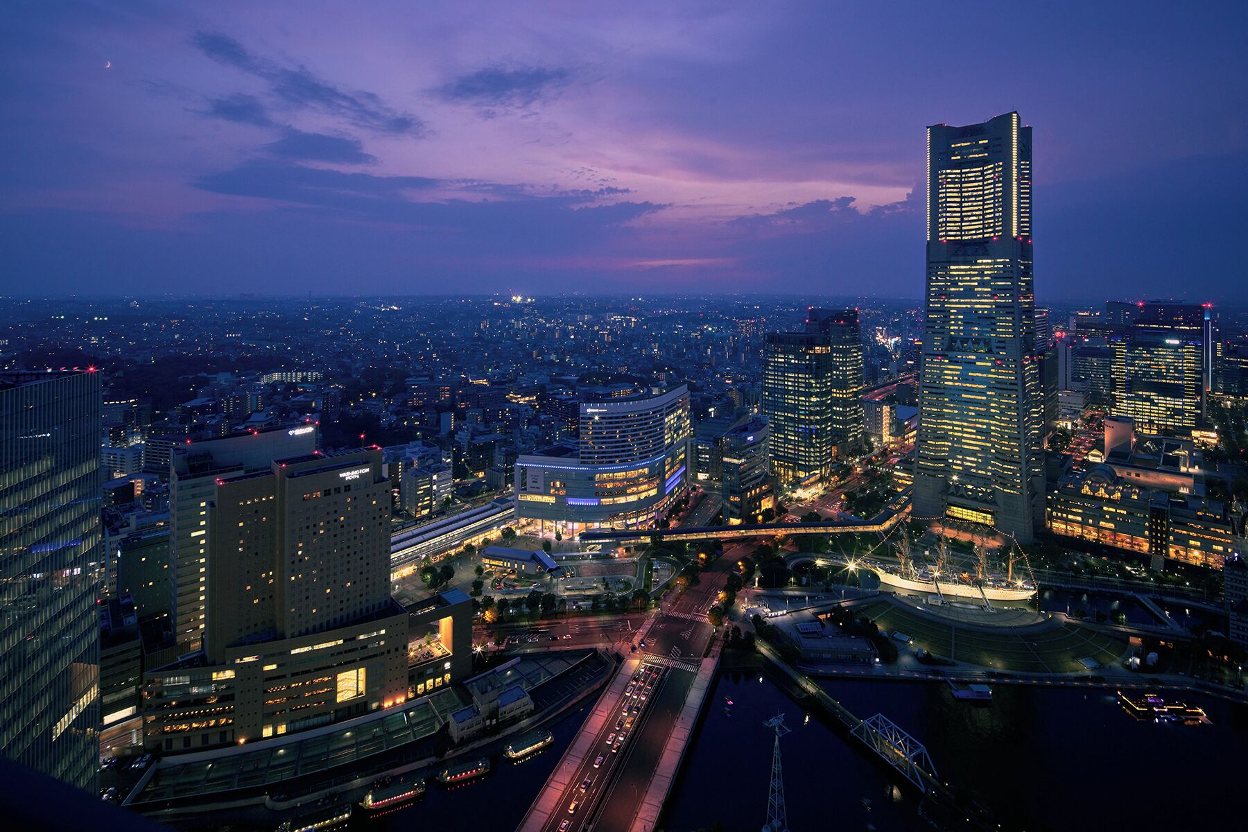 A nighttime cityscape with a prominent skyscraper, a river with bridges, and a mix of high-rise buildings.