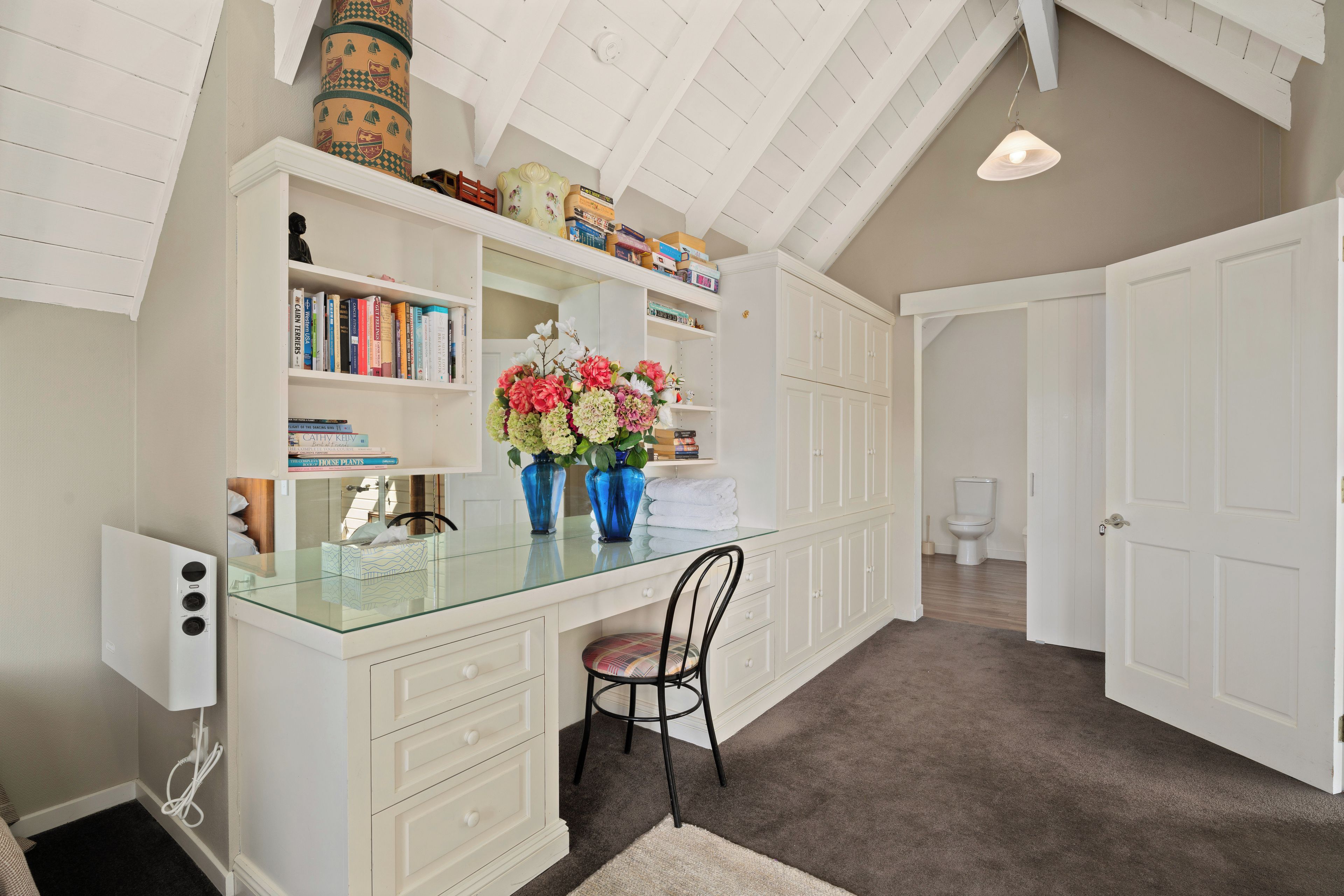 A spacious room with a high ceiling, a glass desk, a chair, and a white wardrobe.