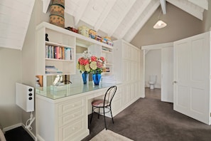 A spacious room with a high ceiling, a glass desk, a chair, and a white wardrobe.
