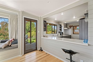 A modern kitchen with a large window, sliding glass door to a deck, and a built-in bench with cushions.