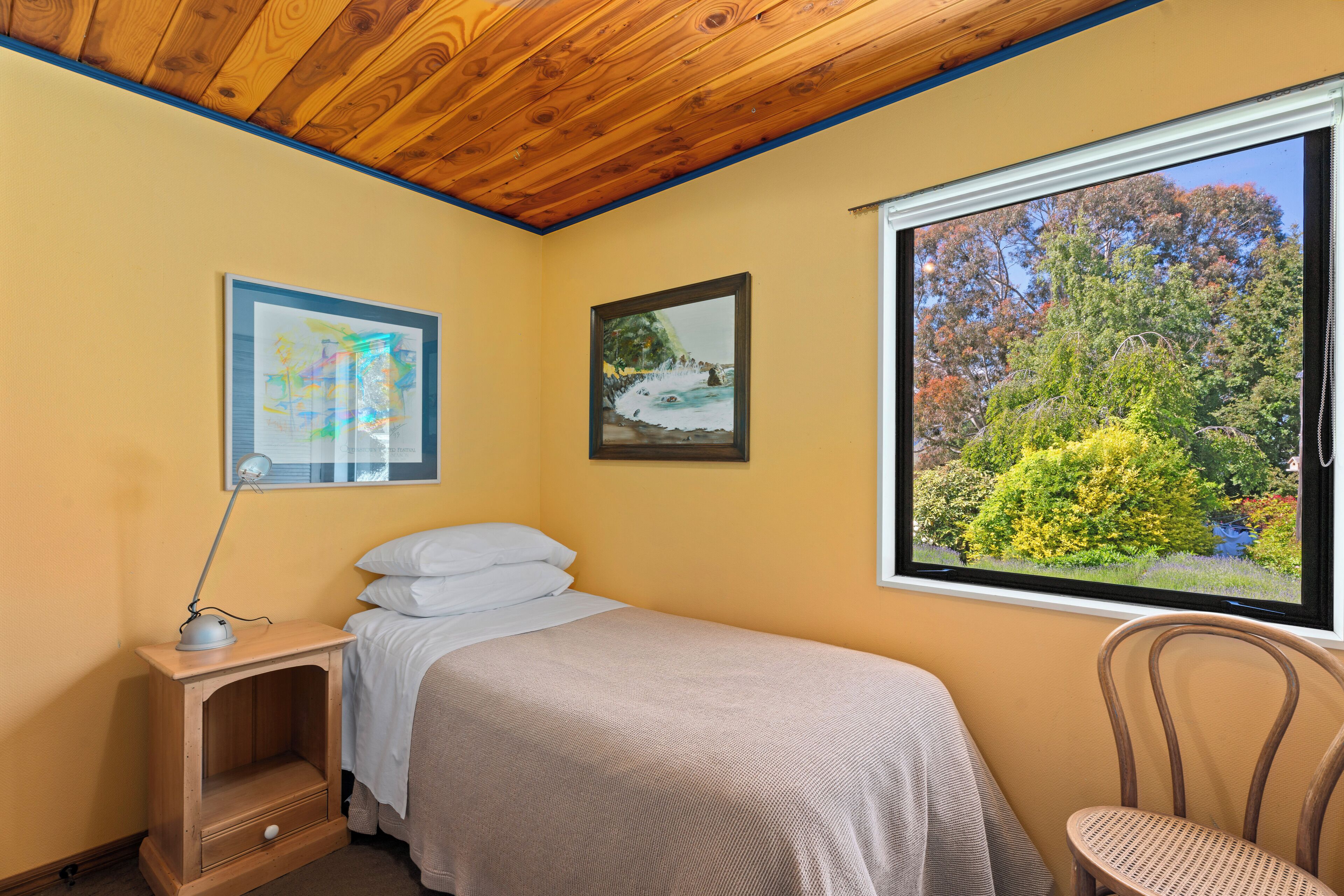 A bedroom with a bed, a nightstand, a chair, and a window with a view of trees and a lake.