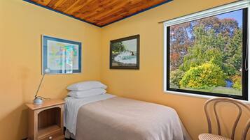 A bedroom with a bed, a nightstand, a chair, and a window with a view of trees and a lake.