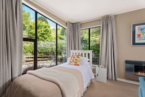 A bedroom with a large window, a bed, a bedside table, and a fireplace.