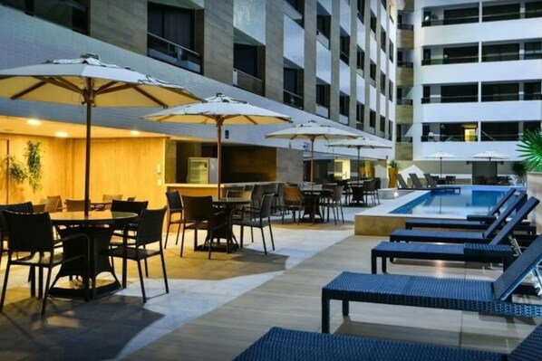 A hotel lobby with a pool area, outdoor seating, and umbrellas. - Nomar XIX (João Pessoa)