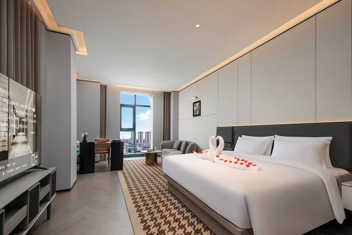A modern hotel room with a large bed, a desk, and a view of the city.