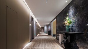 A modern hotel corridor with a patterned floor, a reception desk with a vase of flowers, and a dark wall with a textured finish. - KUNSHANKAICHENJIUDIAN (Suzhou)