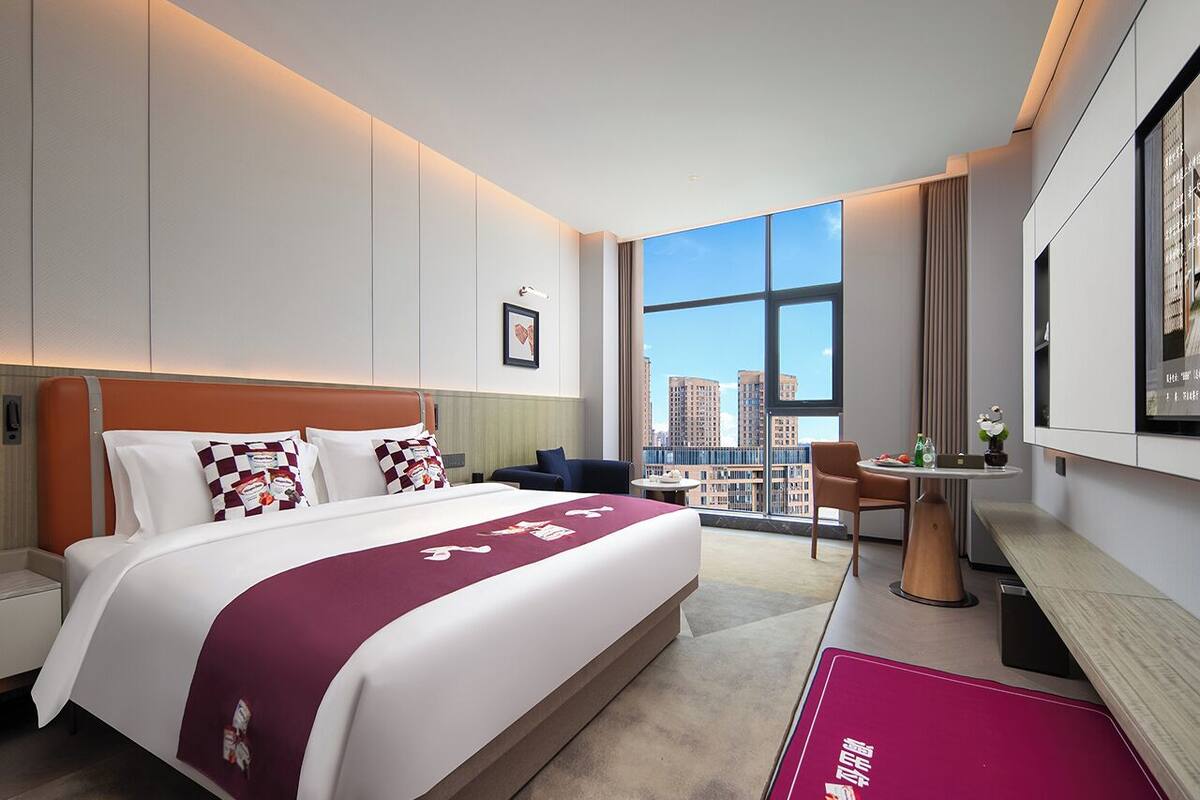 A modern hotel room with a large bed, a desk, and a view of the city.