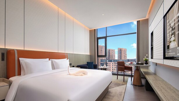 A modern hotel room with a large bed, a desk, and a view of the cityscape. - KUNSHANKAICHENJIUDIAN (Suzhou)