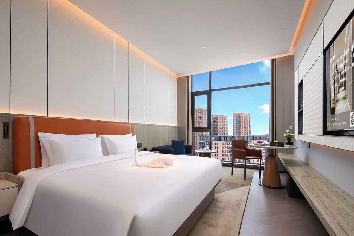 A modern hotel room with a large bed, a desk, and a view of the cityscape.