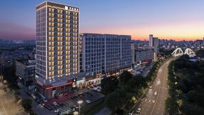 A high-rise hotel with multiple floors, a parking lot, and a bridge in the background. - KUNSHANKAICHENJIUDIAN (Suzhou)