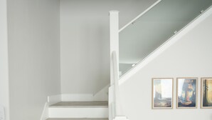 A staircase with white steps and a white handrail, leading to a landing with a white bench and three framed pictures on the wall.