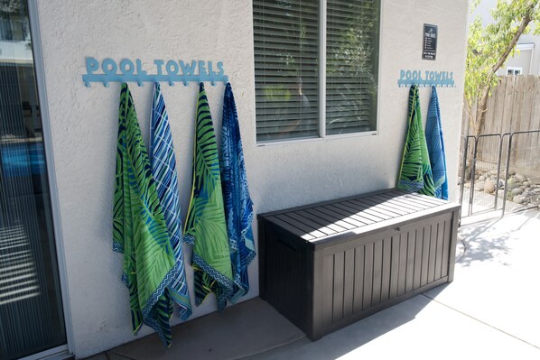 Zona de piscina con toallas colgadas en una pared y un banco de madera.