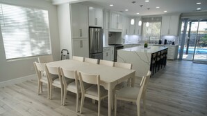 A modern kitchen with white cabinetry, a central island, and a dining area with a white table and chairs.