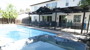 A backyard with a swimming pool and hot tub, surrounded by a fenced patio area with outdoor furniture.