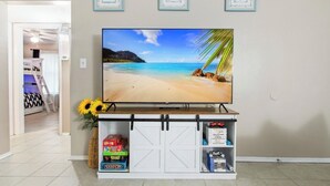 A TV on a stand with a beach scene, a white cabinet with storage, and a door leading to another room.