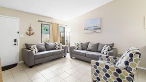 A living room with two grey sofas, a patterned armchair, a painting, and a decorative anchor on the wall.