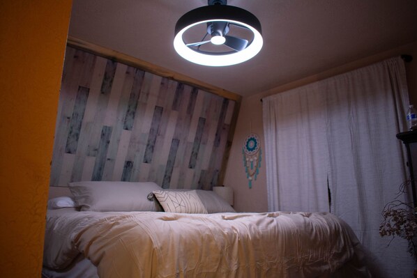 A bedroom with a wooden headboard, a bed with white bedding, a ceiling fan, and a dreamcatcher decoration.