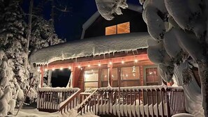 A snow-covered building with a wooden exterior, a porch, and a staircase leading to the entrance.