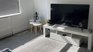 A modern living room with a large flat-screen TV, a white entertainment unit, a small round table with chairs, and a radiator.