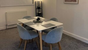 A dining area with a white table, four grey chairs, a black floor lamp, and a radiator.