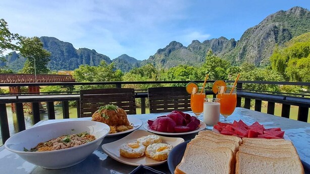 Ein Tisch im Freien mit Blick auf die Berge, mit einer Nudelschüssel, einem Eierteller, Wassermelonenscheiben und Gläser Orangensaft.