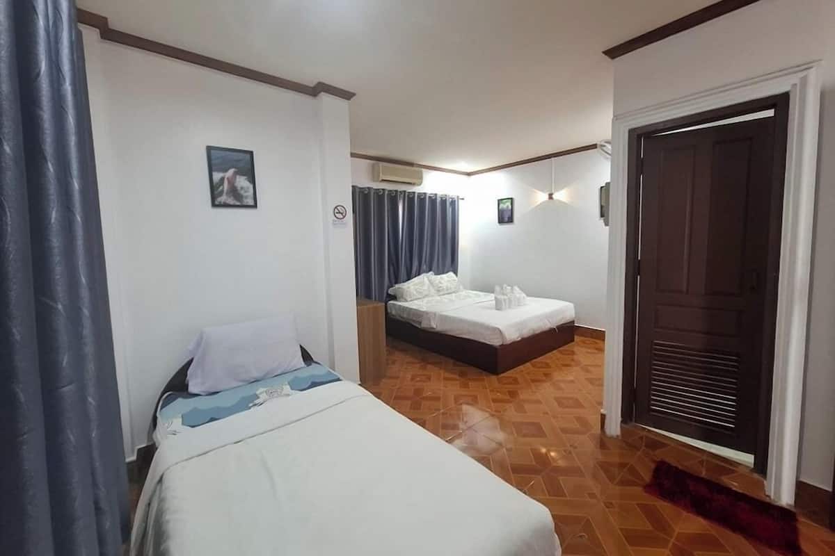 A hotel room with two beds, a wooden floor, a door, and a curtain.