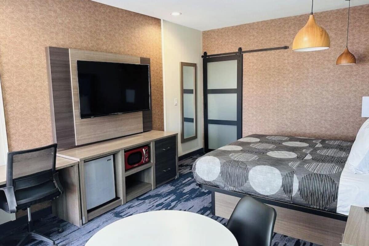 Une chambre d’hôtel moderne dotée d’une télévision à écran plat, d’un placard avec porte coulissante, d’un coin repas et d’une couvre-lit à motifs.