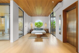 A modern bedroom with a wooden ceiling, a circular skylight, a bed, bedside tables, and a large window.