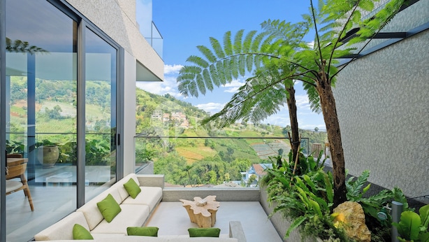 A modern balcony with a glass wall, a white sofa with green cushions, a wooden coffee table, and a fern plant. - Dago Escape Villa by Kozystay - Bandung (Cimenyan)