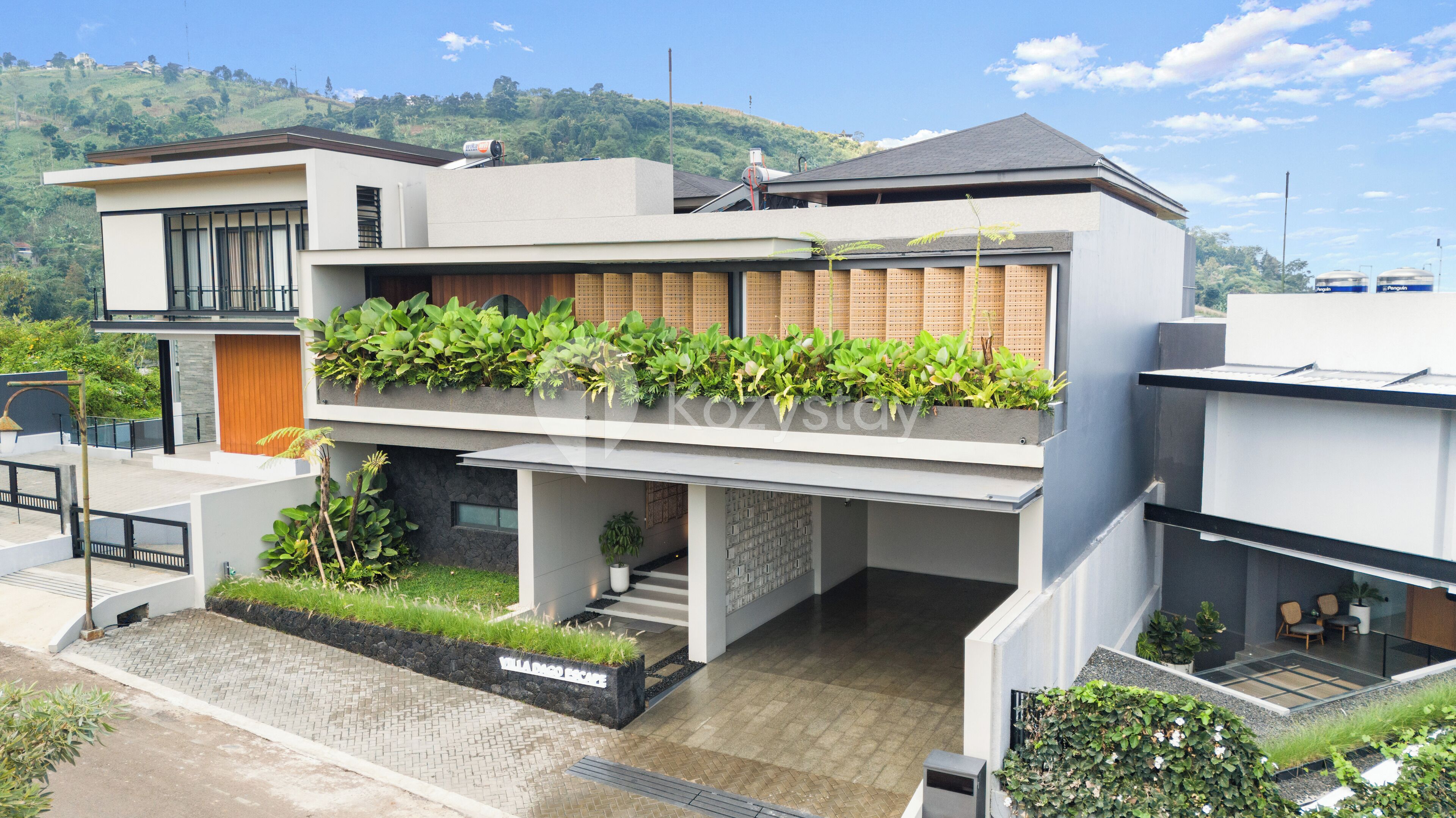 Uma casa moderna de dois andares com telhado plano, janelas amplas e varanda com plantas.