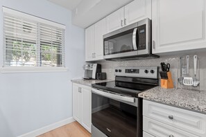 Una cocina con gabinetes blancos, microondas, estufa y cafetera.