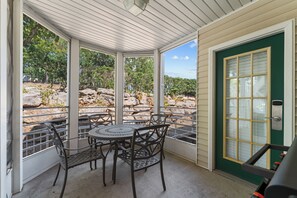 A covered patio with a table and chairs, a green door, and a view of a rocky landscape.