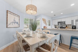 Un coin repas avec une table dressée pour quatre personnes, une cuisine équipée d’appareils électroménagers modernes et une carte encadrée accrochée au mur.