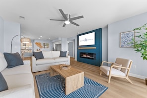 Un salon moderne avec un canapé blanc, une table basse en bois, un tapis à motifs bleus, un fauteuil beige et une cheminée.