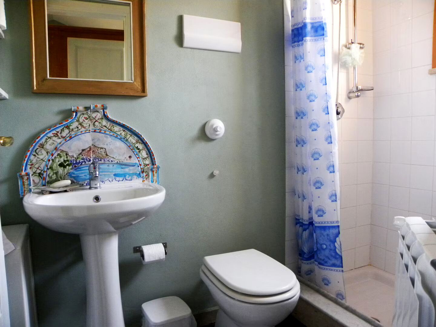 Een badkamer met een betegelde douche, een witte wastafel met decoratieve spatplaat, een toilet en een spiegel boven de wastafel.