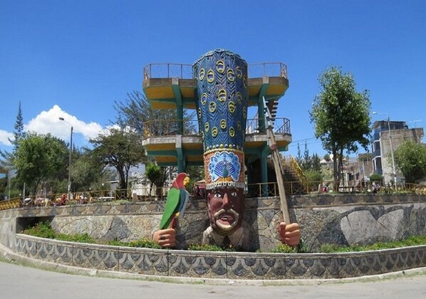 Una gran escultura colorida con diseño de pavo real, un hombre sosteniendo un objeto verde, y una estructura circular con escaleras.