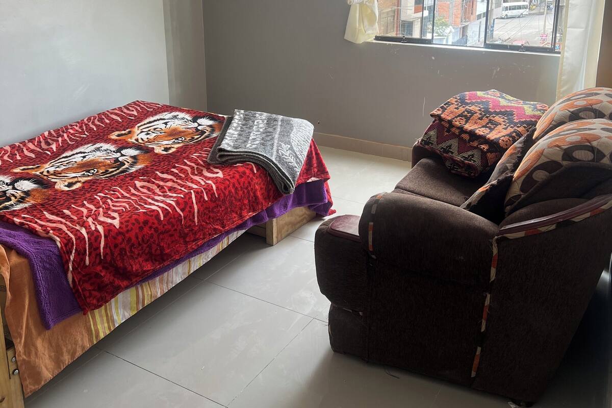 A room with a bed, a sofa, and a window with a view of buildings.