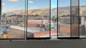 Vista da janela, com moldura de metal, sobre a paisagem urbana com edifícios e montanhas ao longe.