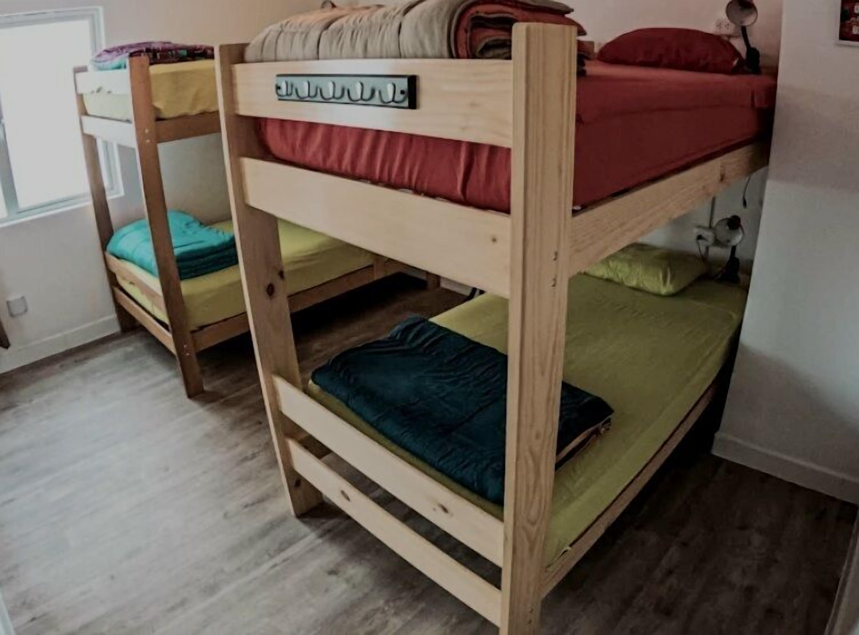 A bunk bed with a label on the top bunk, a window with blinds, and a wooden floor.