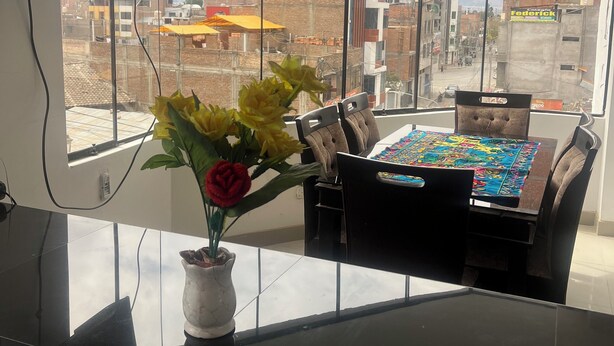 Uma cozinha moderna com uma janela grande, uma área de jantar com mesa e cadeiras, e um vaso com flores no balcão.