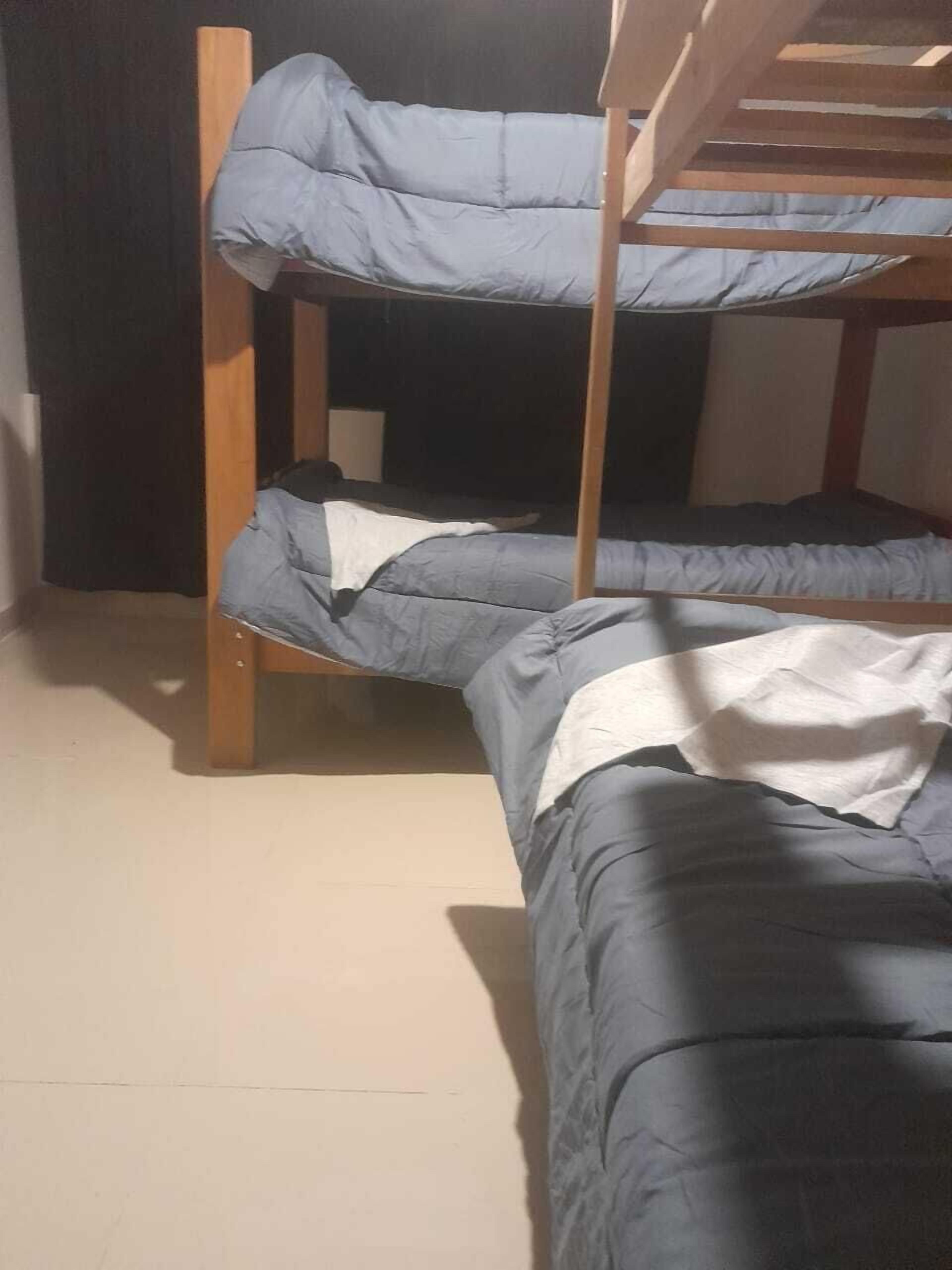 Una cama litera con dos niveles, estructura de madera y ropa de cama gris.